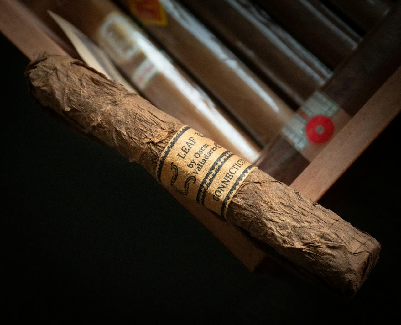 about-us Detailed view of a hand-rolled cigar with label, set in a wooden cigar box.